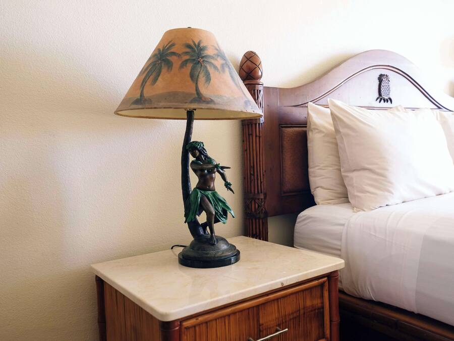 A bed with white bedding, a wooden headboard, and a nightstand with a lamp and a statue.