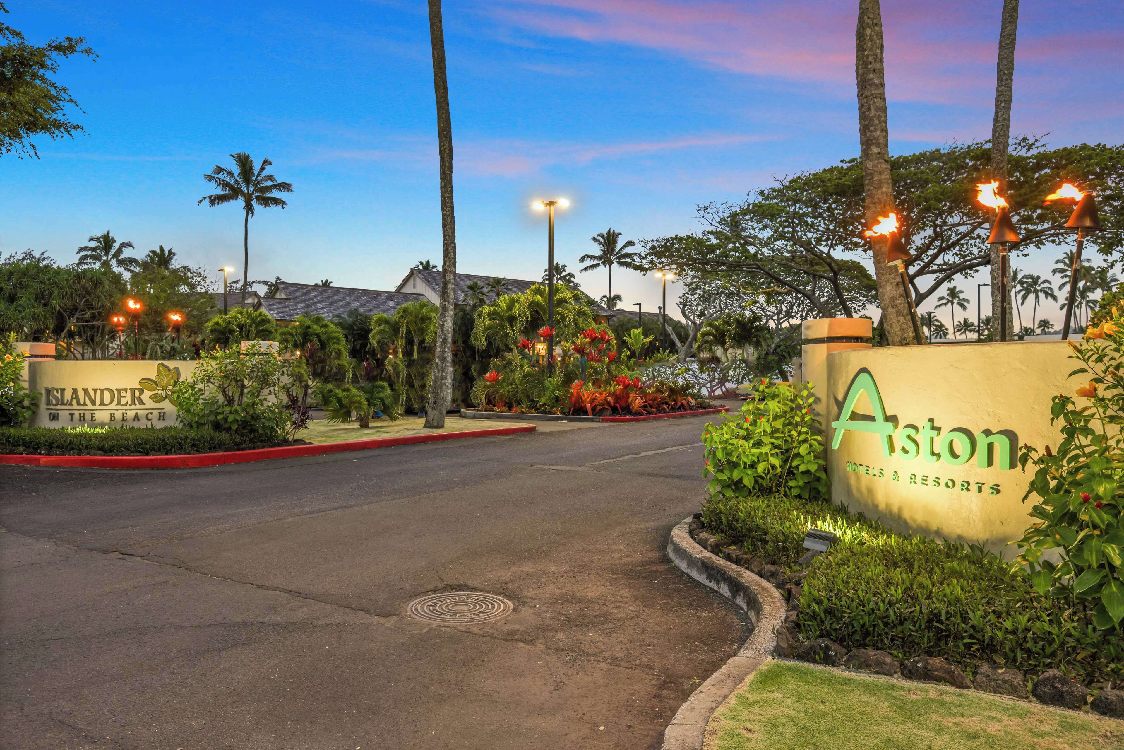 A hotel entrance with palm trees, a landscaped garden, and a sign for 'Aston Hotels & Resorts'.