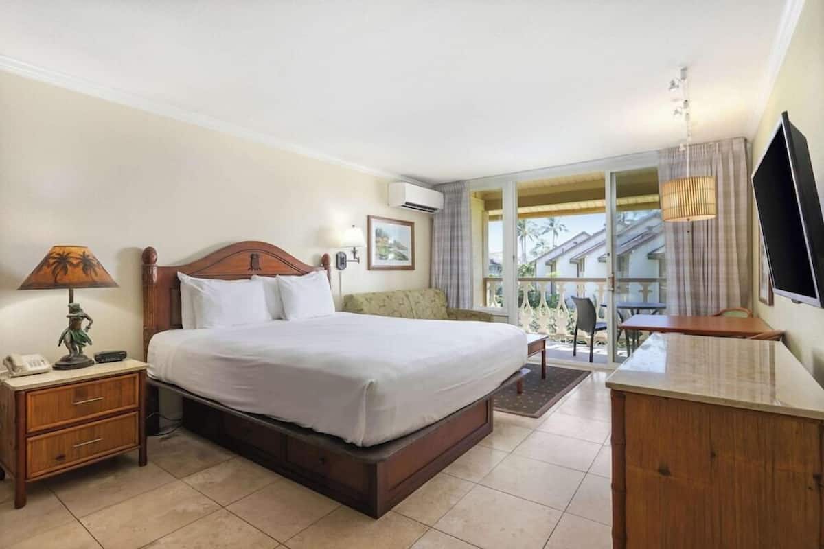Habitación de hotel con cama, escritorio, silla, televisor y ventana con vistas a edificios.