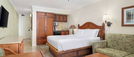 A hotel room with a bed, a sofa, a wooden desk, a ceiling fan, and a kitchenette.