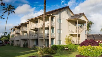 A multi-story hotel with balconies, a well-maintained lawn, and tropical landscaping.