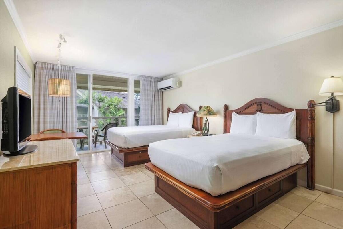 Una habitación de hotel con dos camas, un escritorio, un televisor y una ventana con cortinas.
