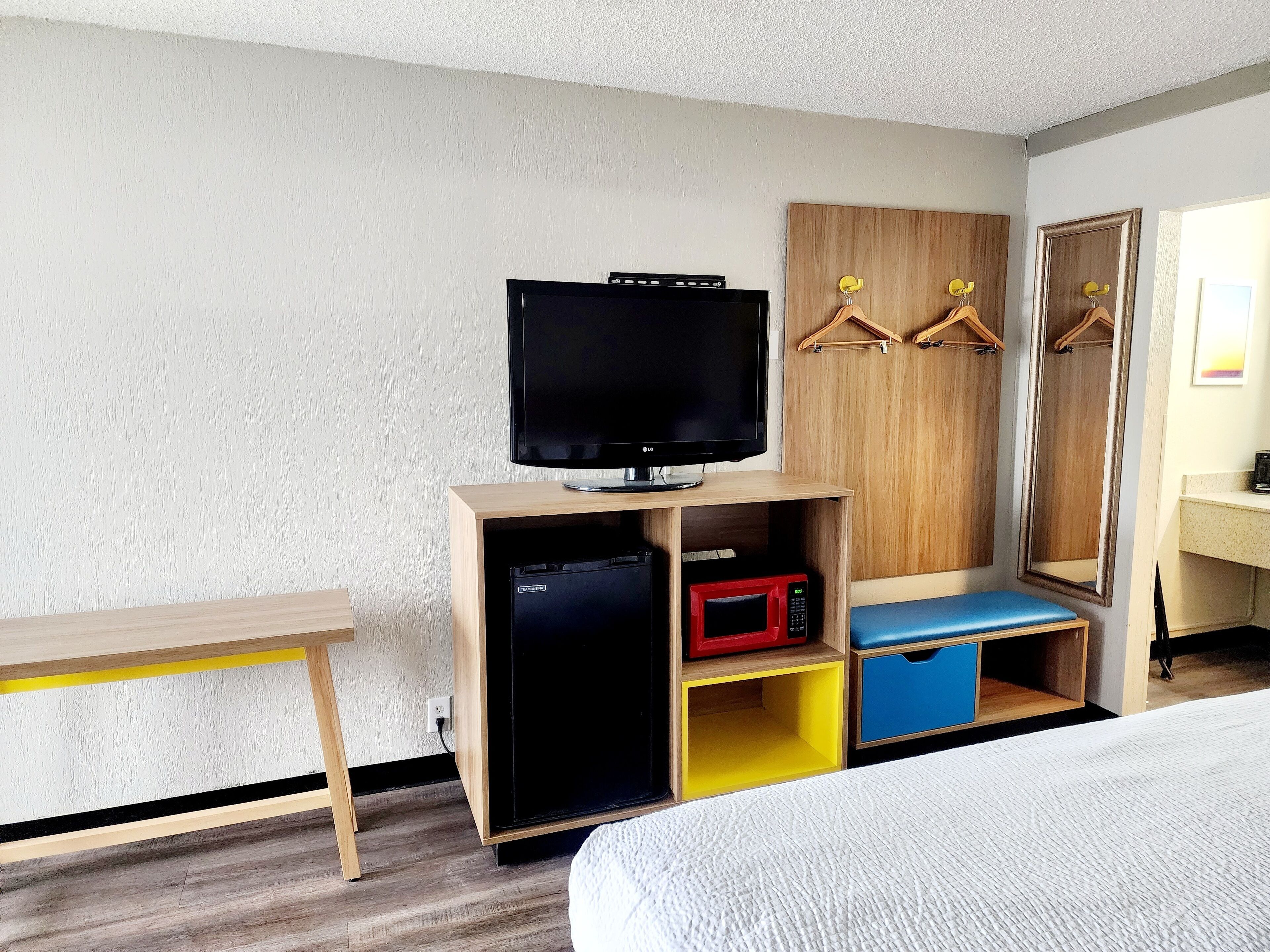 Habitación de hotel con cama, televisor sobre un soporte de madera, microondas y armario con perchas.