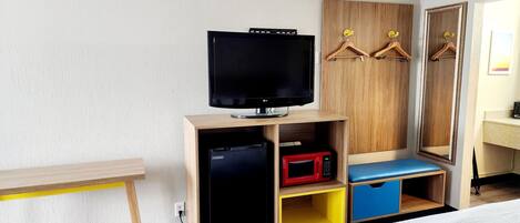 Habitación de hotel con cama, televisor sobre un soporte de madera, microondas y armario con perchas.