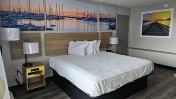 A hotel room with a large bed, wooden headboard, two bedside lamps, a nightstand, and artwork depicting a marina and sunset.