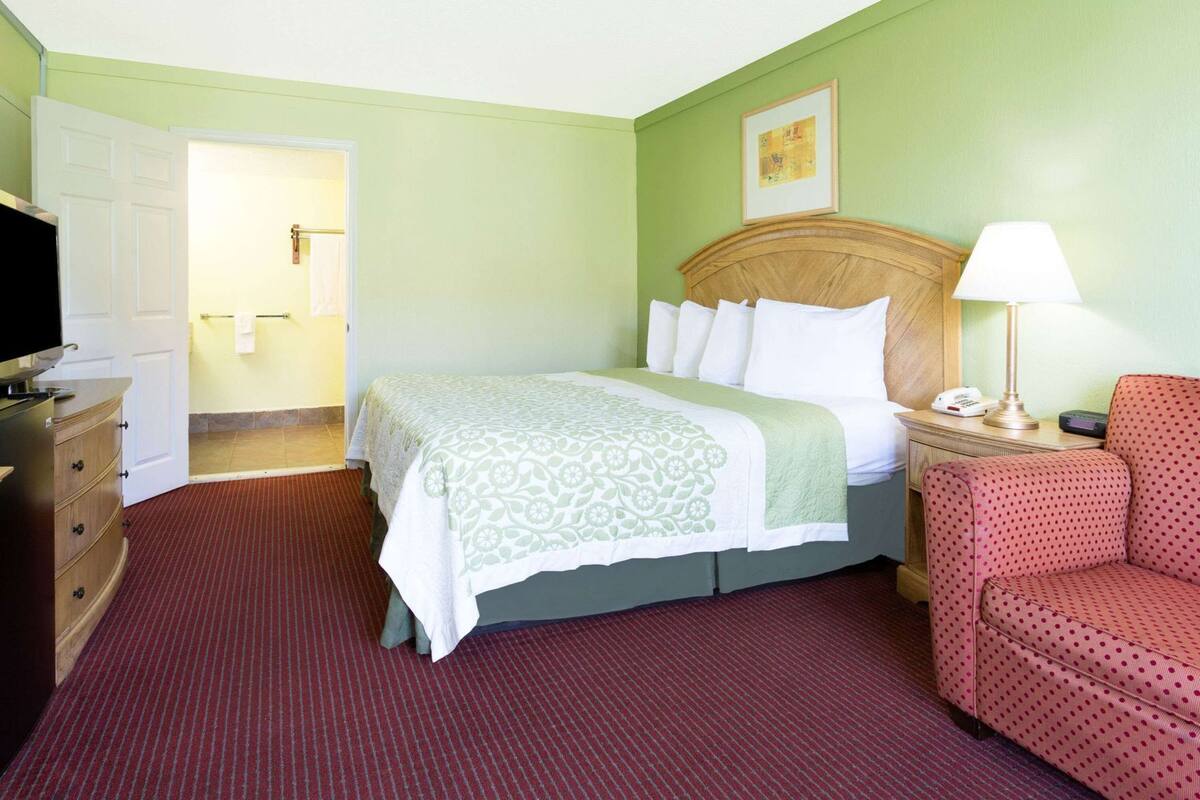 A hotel room with a bed, a chair, a desk with a lamp, and a television.