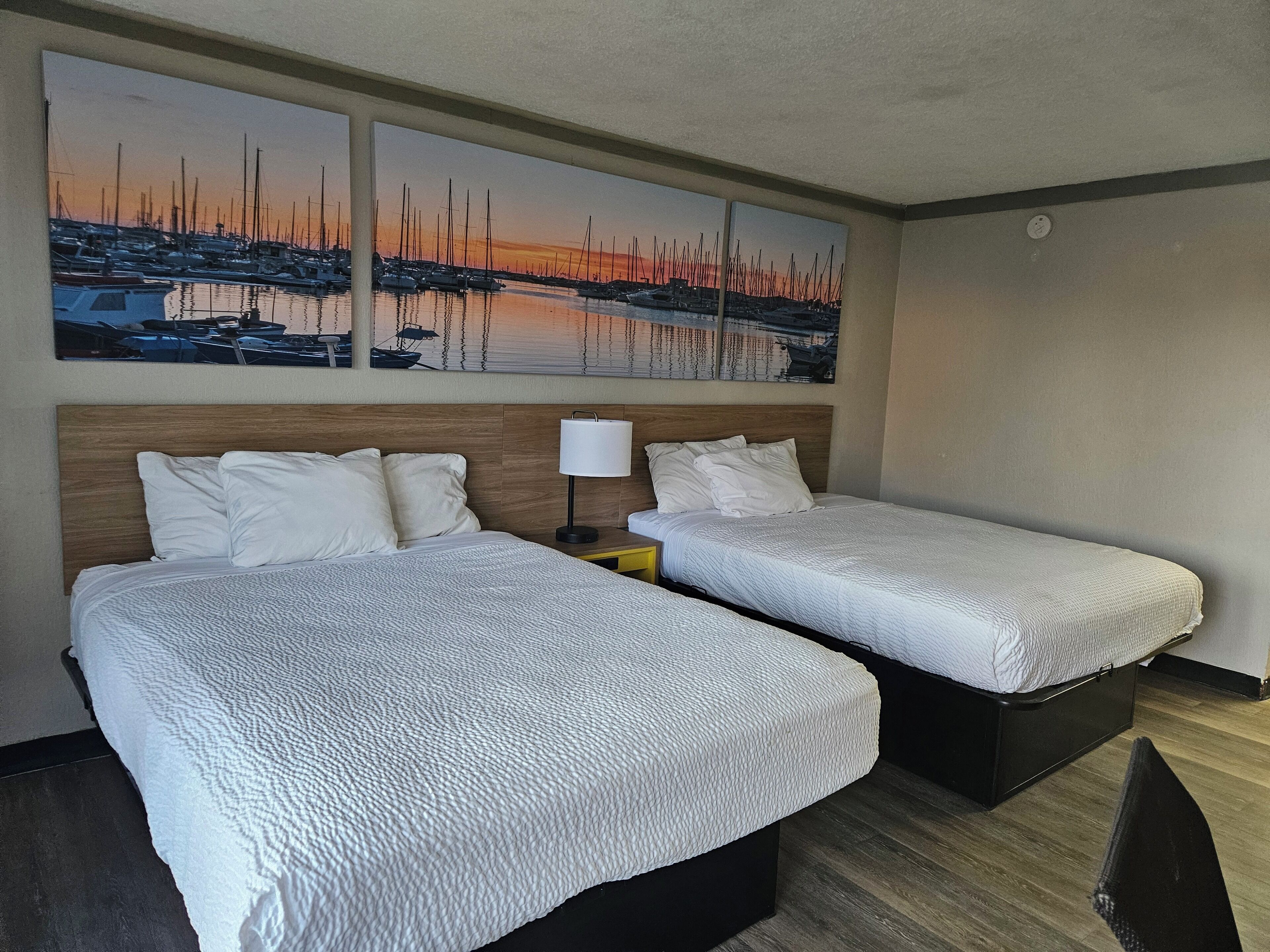 A hotel room with two beds, a nightstand, and a wall-mounted lamp.