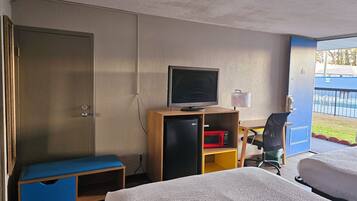 A hotel room with two beds, a desk with a computer and a television, a small refrigerator, and a view of the outside.