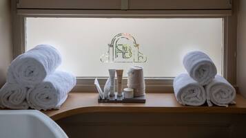 A bathroom with towels stacked on a shelf, toiletries, and a frosted glass window with a logo.