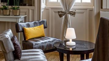 A room with a wooden floor, a black round table with a white lamp, and two leather chairs with yellow and brown cushions.