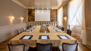 A conference room with a long table, chairs, a projector screen, and wall sconces.