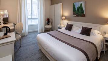 A hotel room with a large bed, bedside tables with lamps, a chair, a desk with a coffee maker, and a painting on the wall.