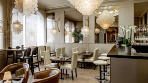 A modern restaurant with high ceilings, chandeliers, and a bar area.