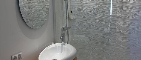 A modern bathroom with a freestanding sink, a shower with a textured wall, and a wooden vanity.