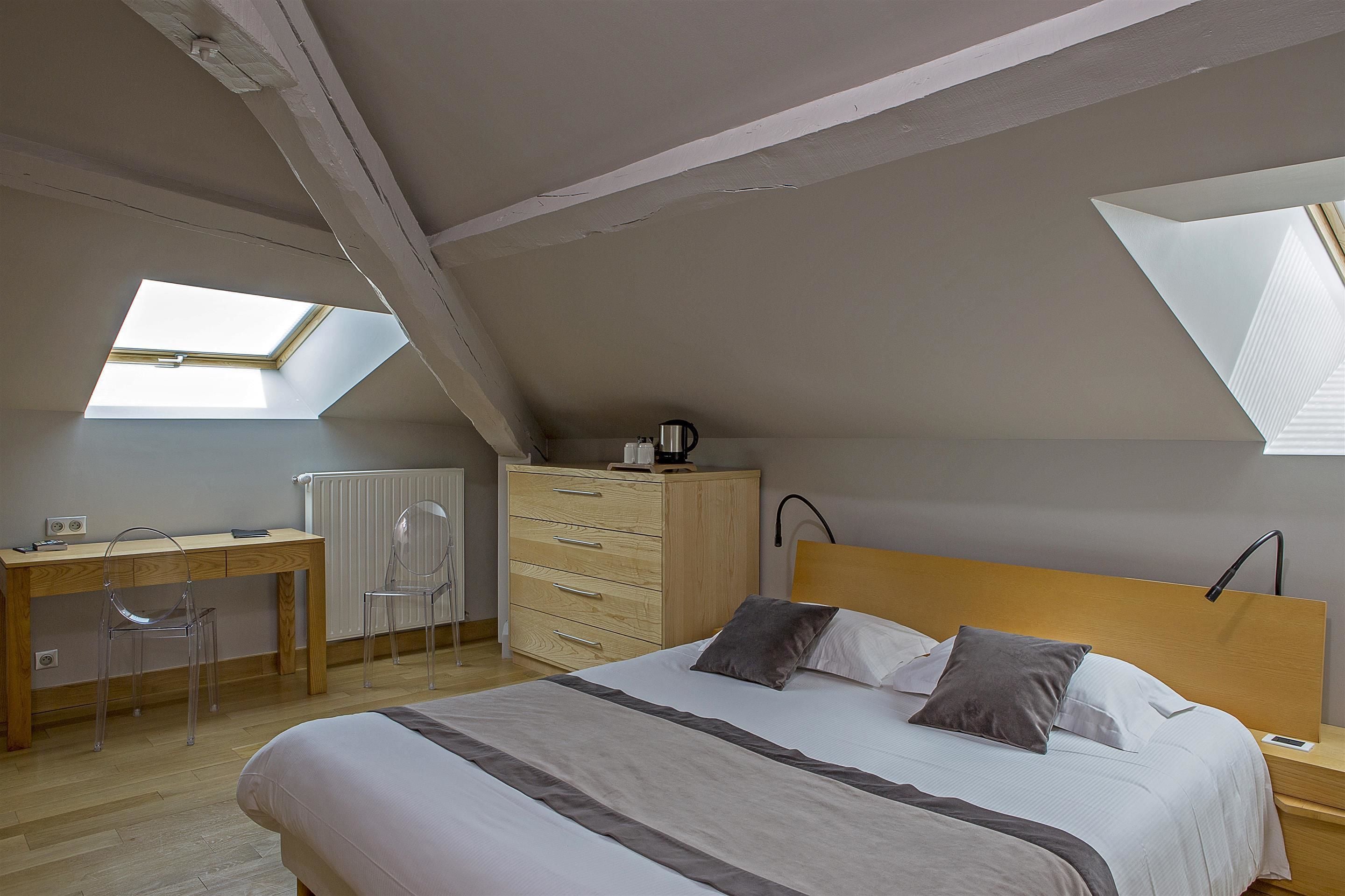 A bedroom with a skylight, a bed with pillows, a desk with a chair, and a dresser.