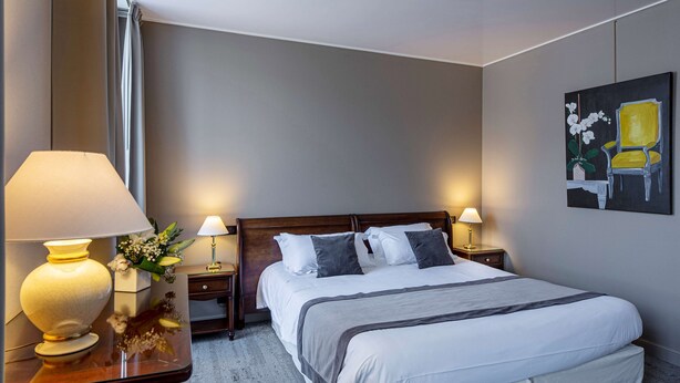 A hotel room with a large bed, two bedside lamps, a nightstand with a lamp, a painting on the wall, and a window with curtains.