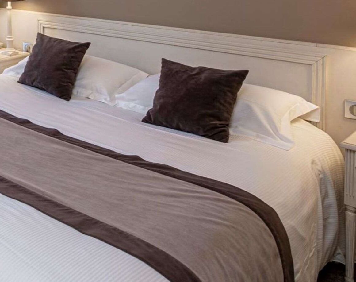 A neatly made bed with a white and brown bedspread, two pillows, and a white headboard.