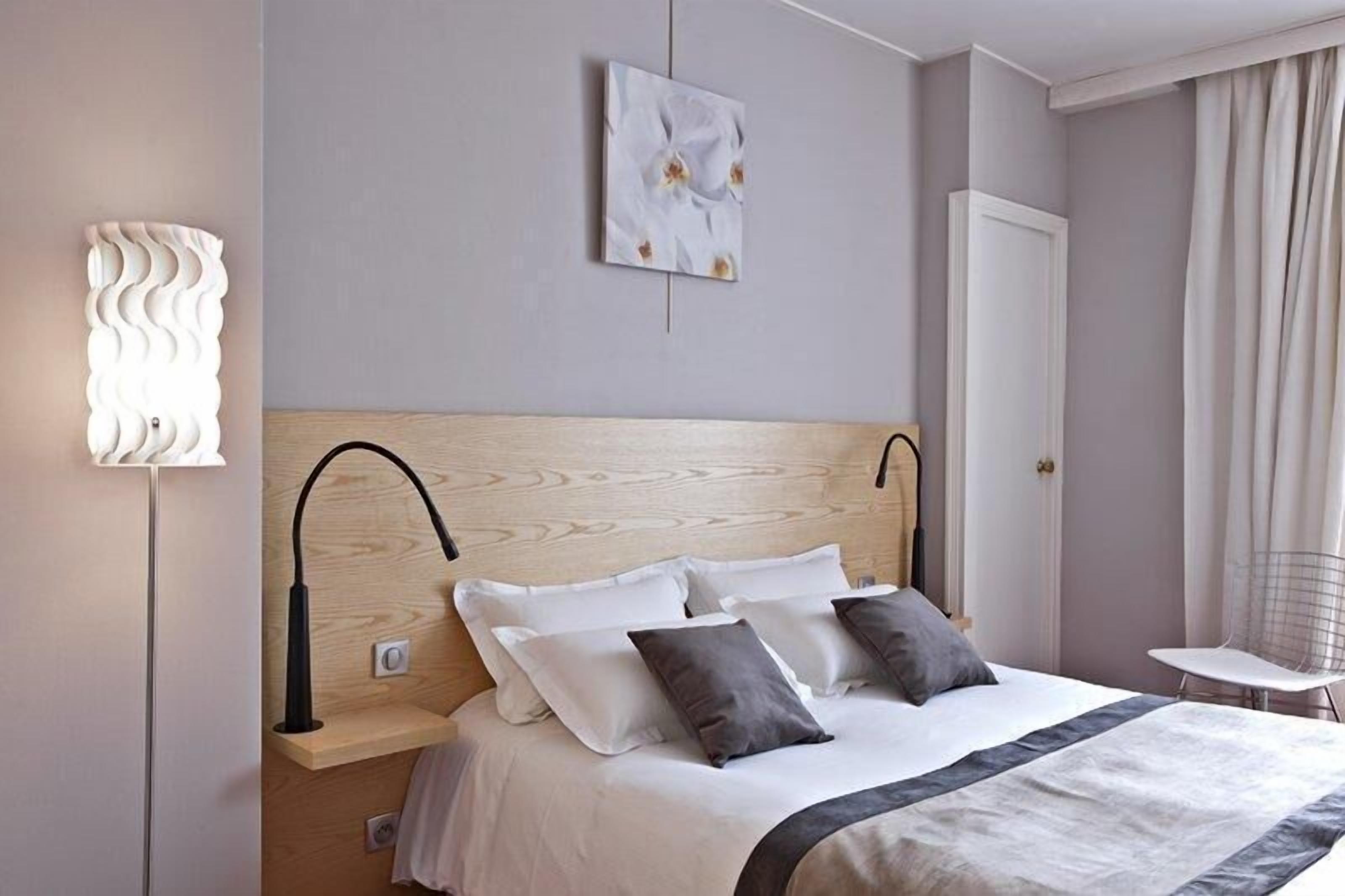 Una cama bien hecha con cabecera de madera, una lámpara de noche y una pequeña mesa con una silla.
