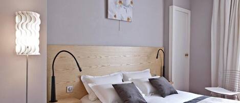 Una cama bien hecha con cabecera de madera, una lámpara de noche y una pequeña mesa con una silla.
