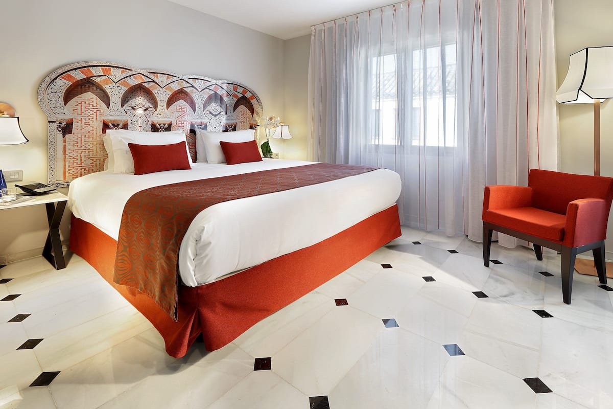 Une chambre d’hôtel avec un grand lit, un fauteuil rouge et une tête de lit décorative.