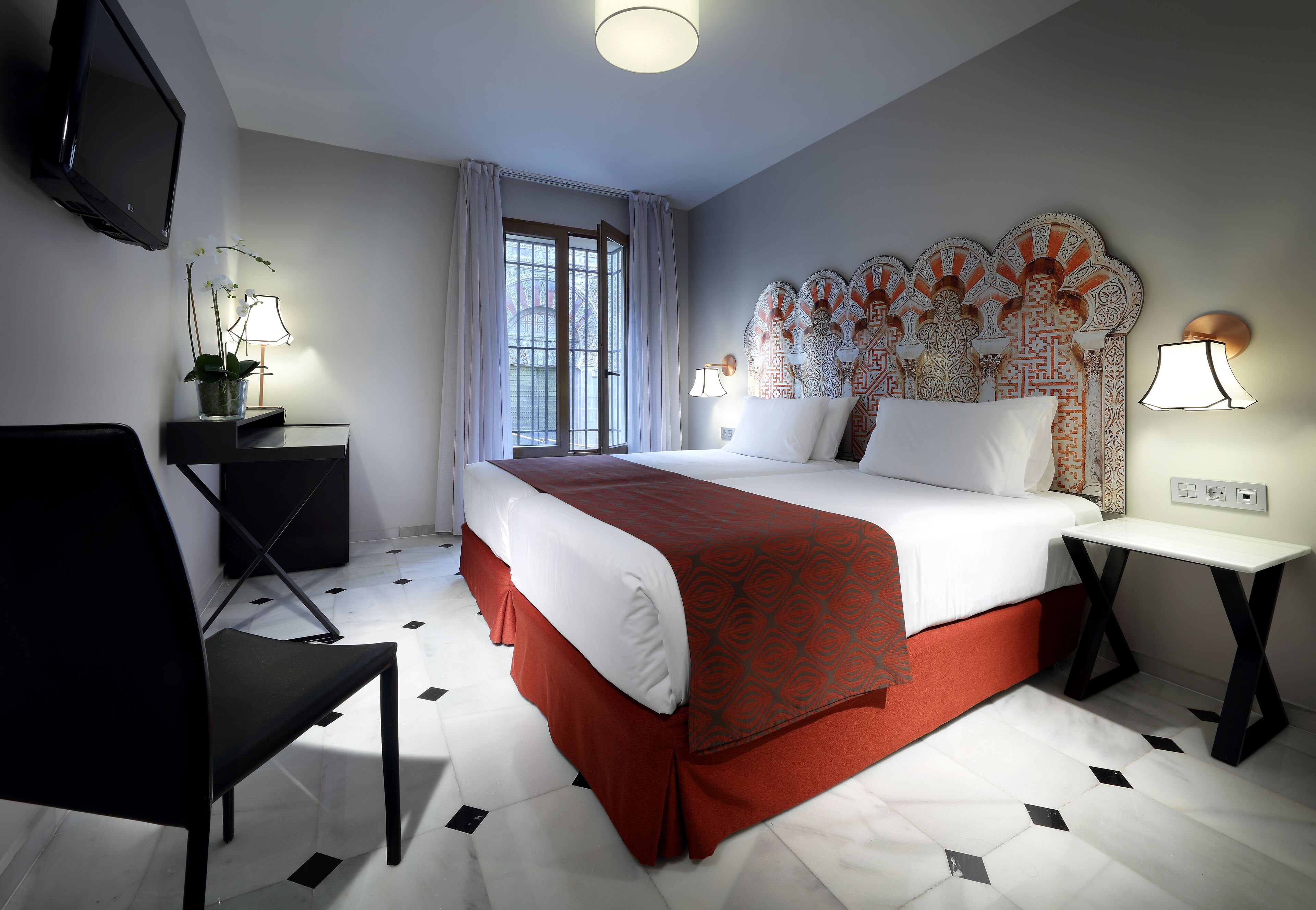 Habitación de hotel con cama, escritorio, silla, televisor y ventana con cortinas.