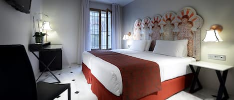 Habitación de hotel con cama, escritorio, silla, televisor y ventana con cortinas.