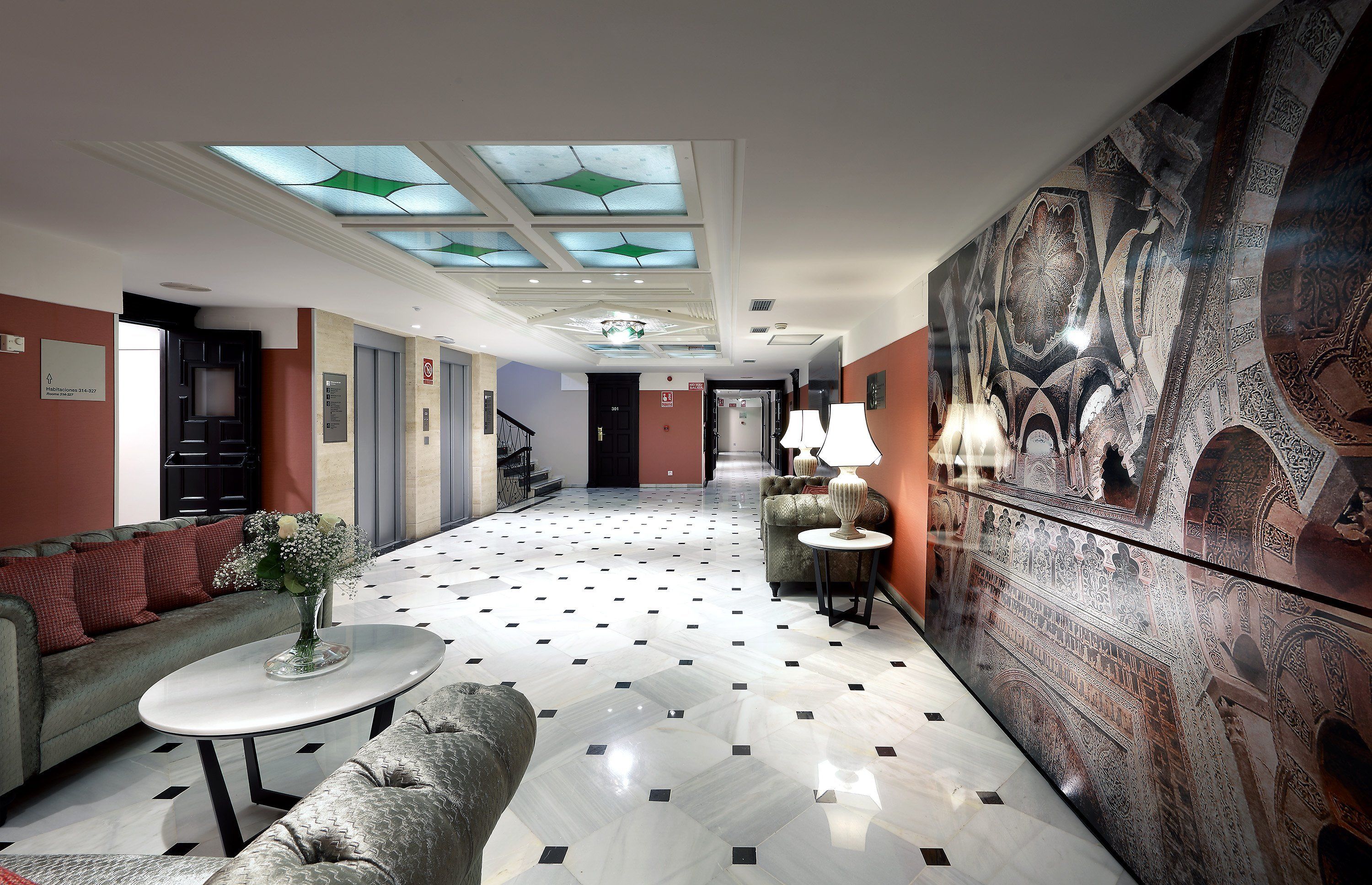 Et hotel lobby med et moderne design, komplet med et mønstret gulv, en sofa, et sofabord, en dekorativ væg og en trappe i baggrunden.