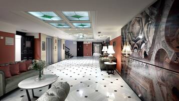Et hotel lobby med et moderne design, komplet med et mønstret gulv, en sofa, et sofabord, en dekorativ væg og en trappe i baggrunden.