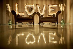 A room with a reflective floor, two sofas, and a large illuminated 'LOVE' sign.