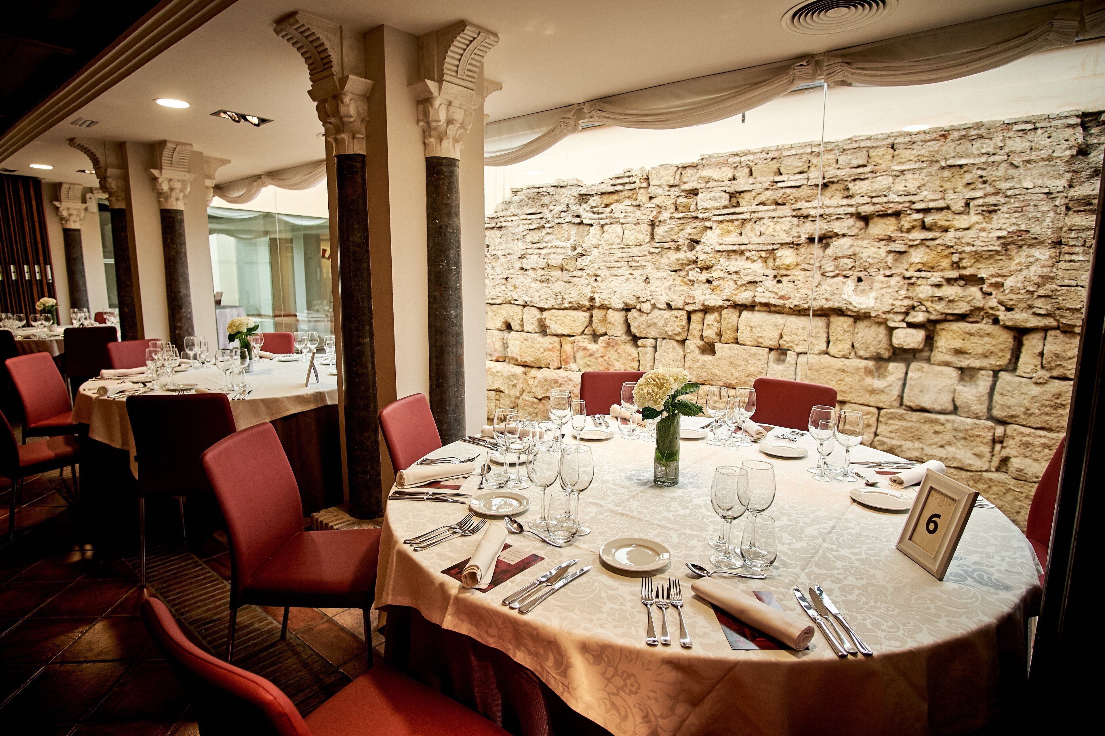 A restaurant with round tables, red chairs, and a stone wall in the background.