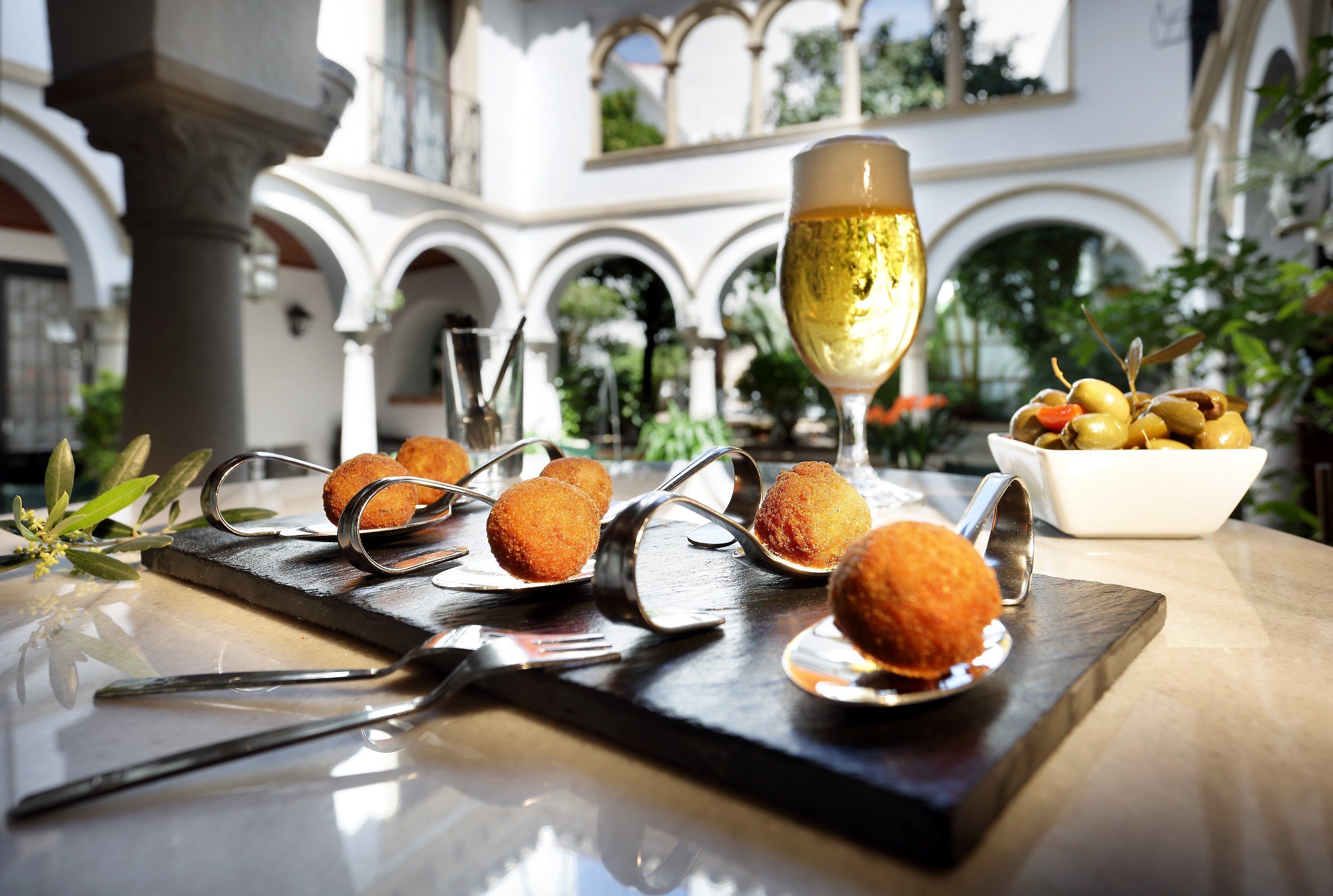 A table with croquettes, a glass of white wine, and a bowl of olives.