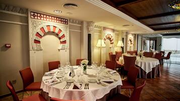Un comedor con mesas redondas dispuestas para cuatro personas, sillas rojas y decoraciones ornamentales en las paredes.