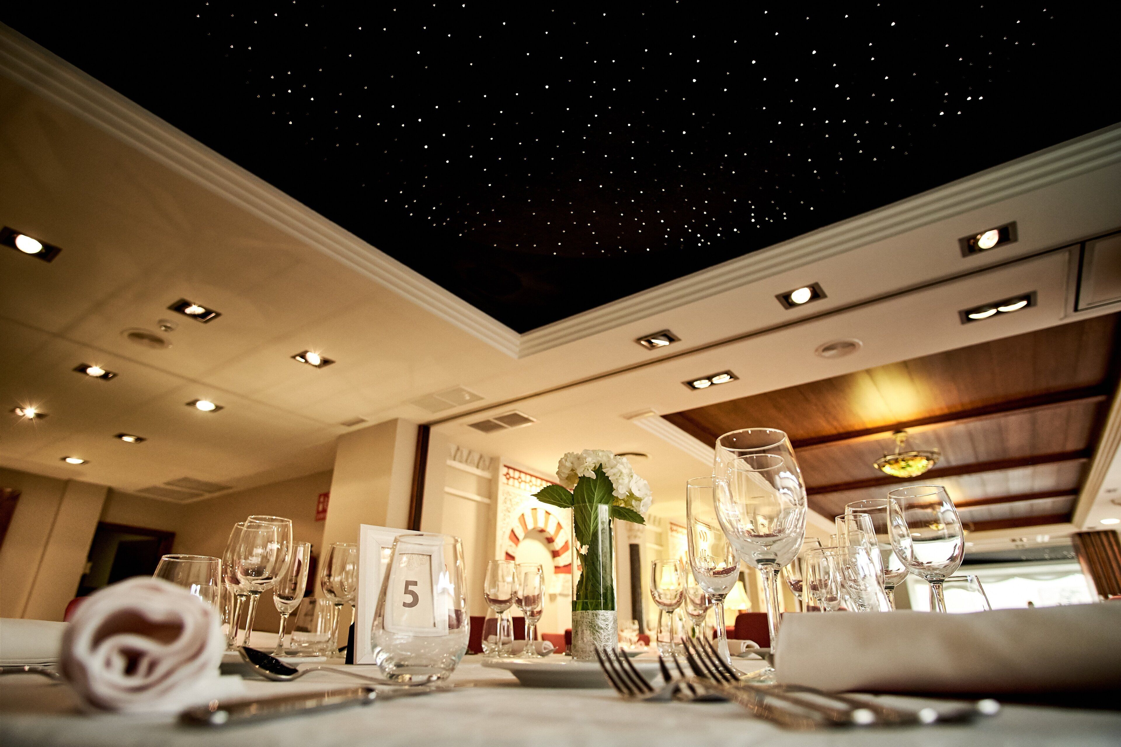 A dining area with a starry ceiling, neatly set tables, and a number '5' sign on the table.