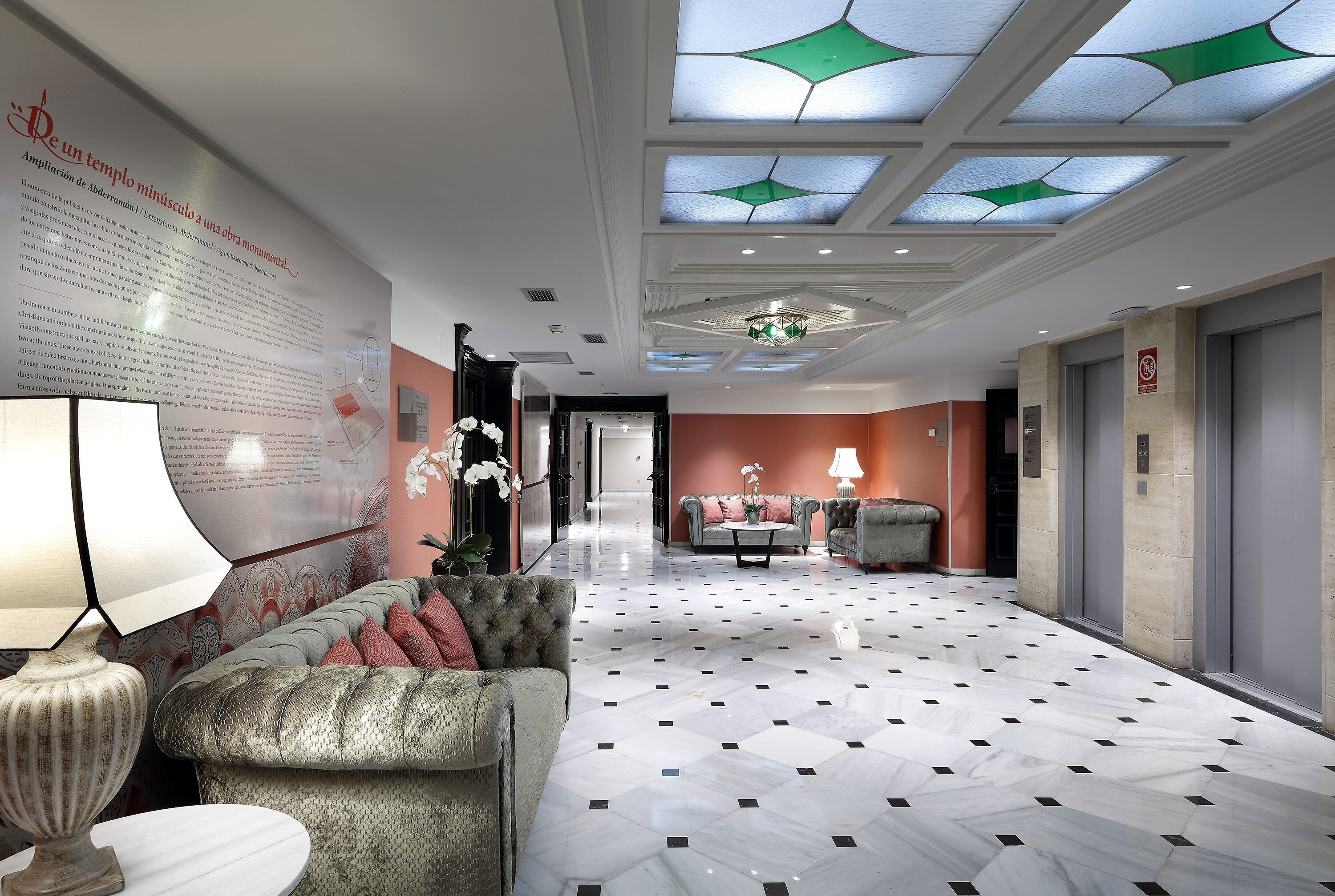 A hotel lobby with a patterned floor, a sofa, a table with a lamp, and a wall with text.