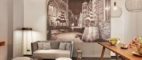Una sala de estar moderna con un sofá, otomanas, una mesa de comedor con un tazón de fruta y un mural grande que representa una escena histórica.