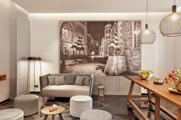 A modern living room with a sofa, ottomans, a dining table with a bowl of fruit, and a large wall mural depicting a historical scene.