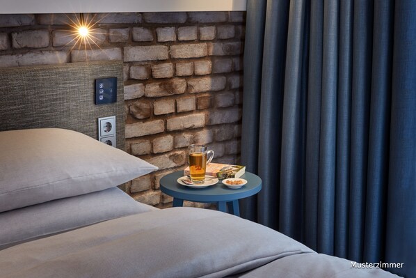 Habitación de hotel con pared de ladrillo, cama con almohadas, una mesita con una bebida y cortinas.