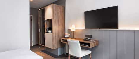 Una habitación de hotel con una cama, un escritorio con silla, un televisor de pantalla plana y un armario.