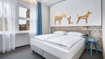 A double bed with white linens, a small blue side table, and a wall-mounted artwork of animals.