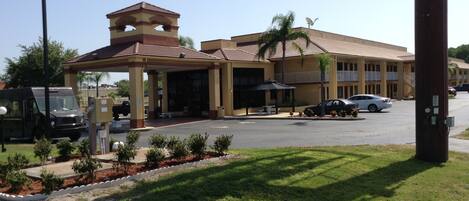 A hotel with a covered entrance, a parking lot, and a small garden area.