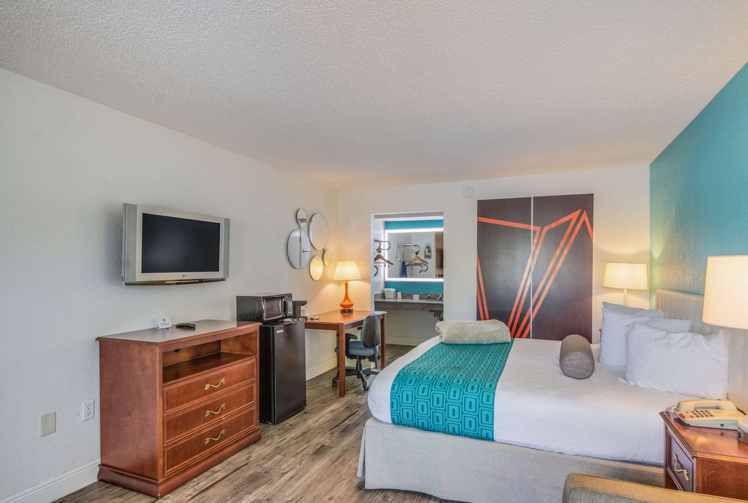 A hotel room with a bed, a desk, a television, a wardrobe, and a bathroom visible through an open door.