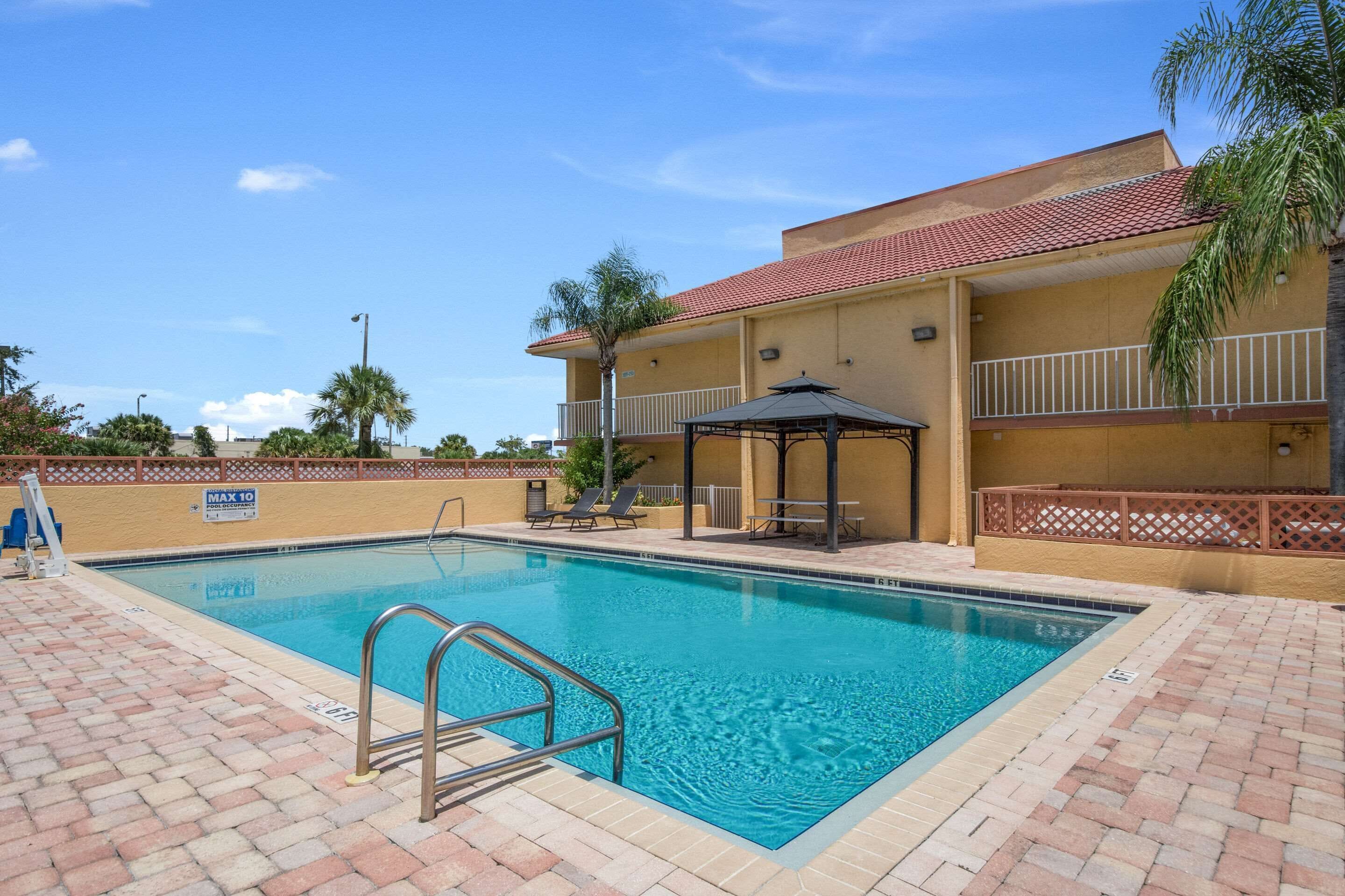 A swimming pool with a metal ladder, lounge chairs, and a covered seating area.