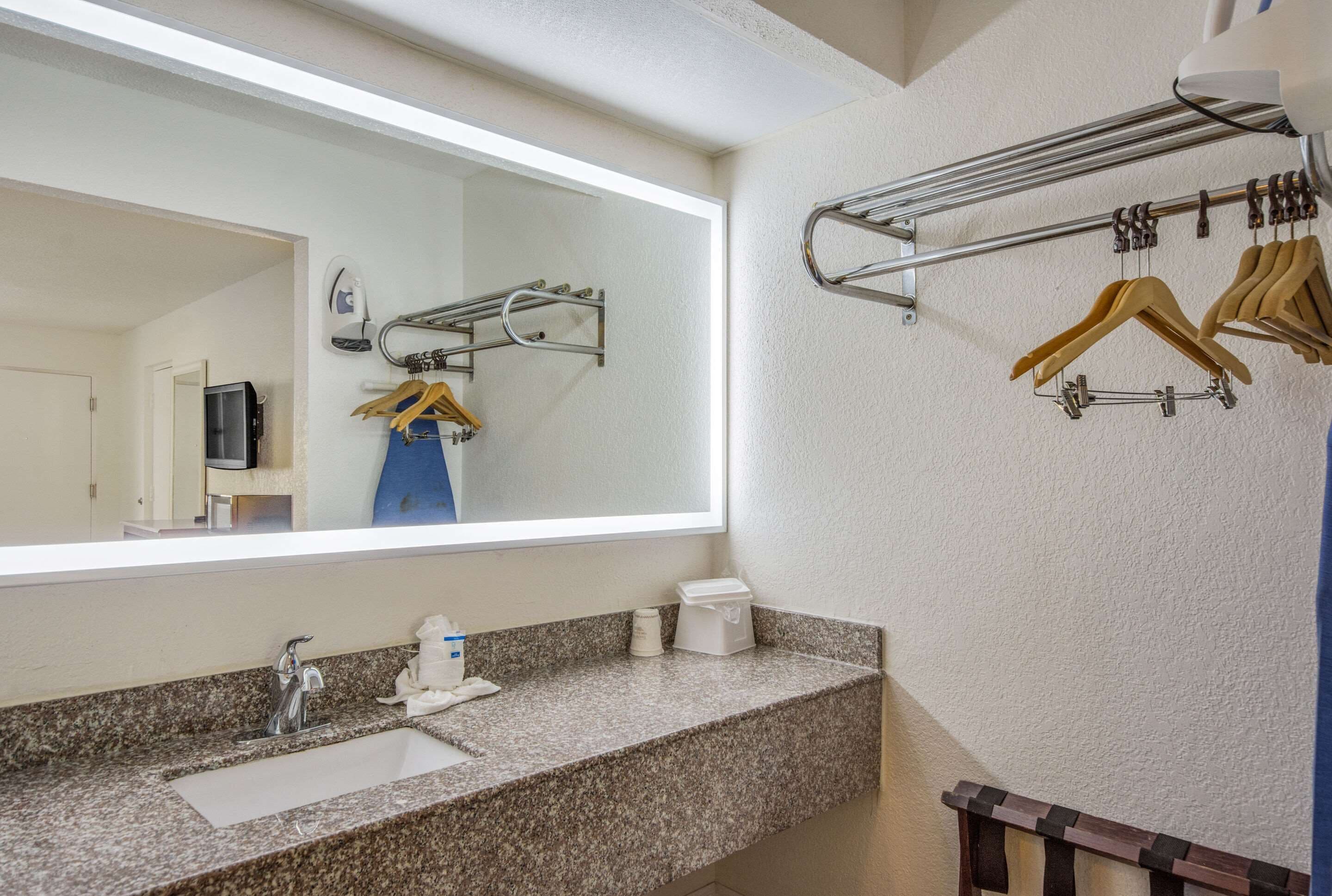 A bathroom with a granite countertop, a sink, a mirror, a towel rack, and a hanging clothes rack.