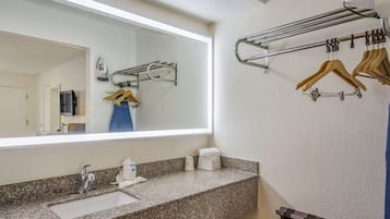 A bathroom with a granite countertop, a sink, a mirror, a towel rack, and a hanging clothes rack.