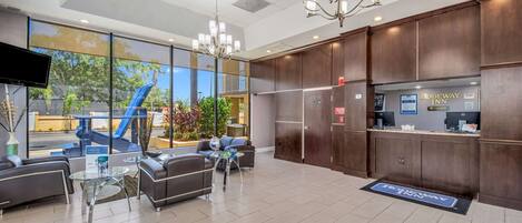 A hotel lobby with seating, a reception desk, and large windows overlooking a landscaped area.