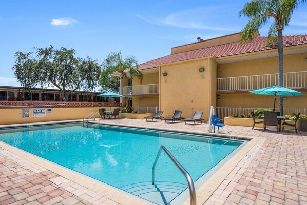 A swimming pool with a metal ladder, lounge chairs, and umbrellas.