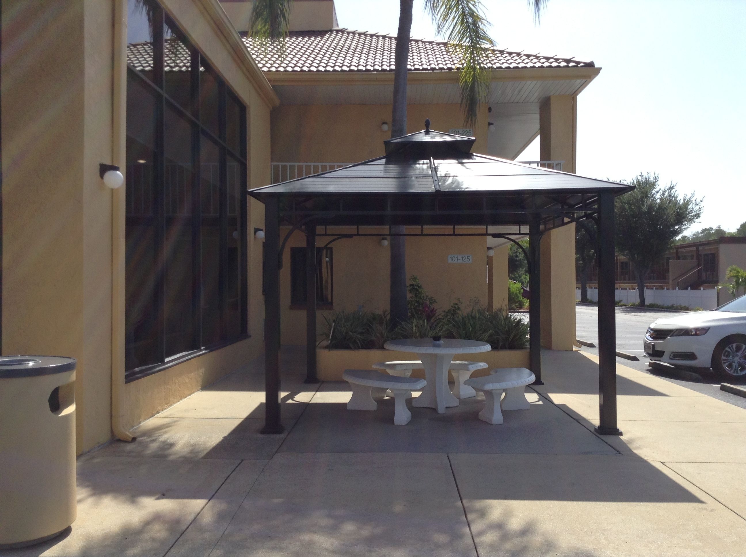 Une terrasse extérieure dotée d’un espace salon couvert, d’une poubelle et d’un bâtiment avec un toit en tuiles.