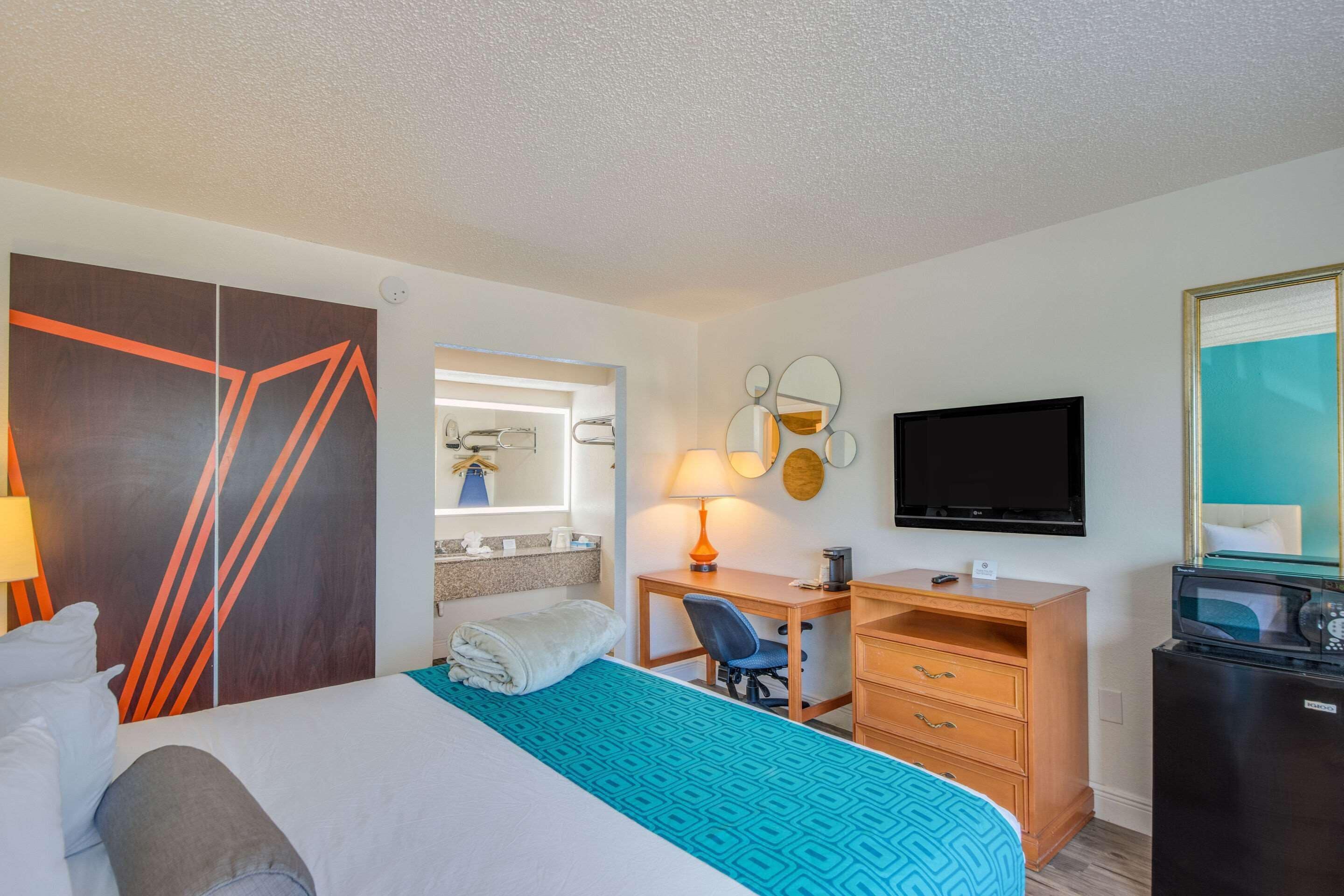 A hotel room with a bed, a desk, a chair, a TV, a mirror, and a wardrobe.