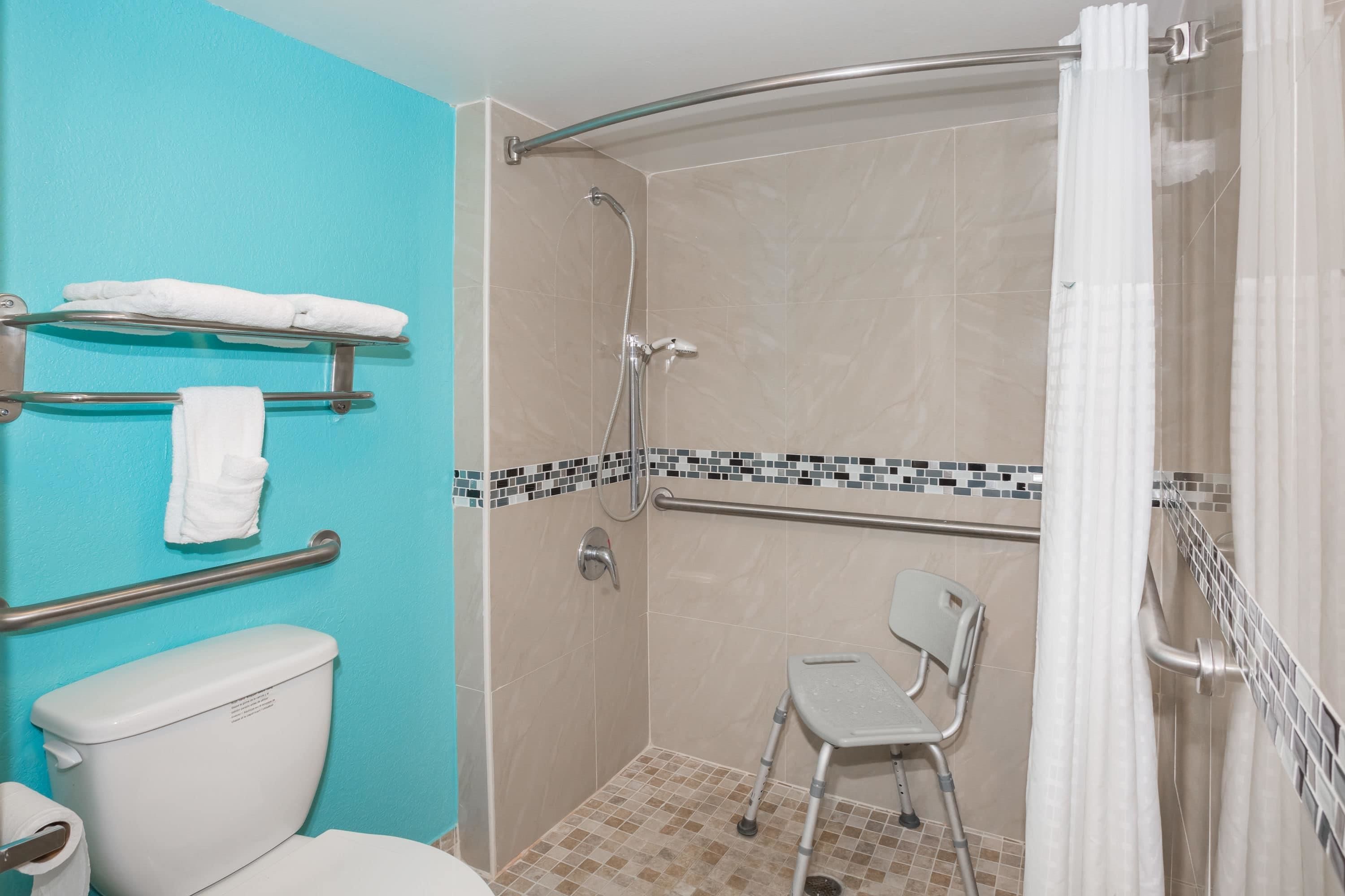 Ducha accesible en silla de ruedas con barra de apoyo, inodoro y silla.