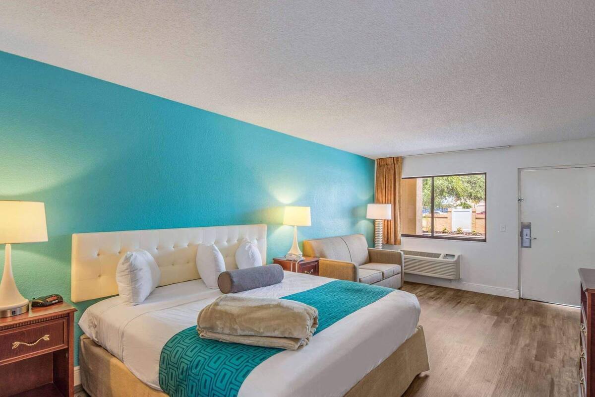 A hotel room with a bed, two bedside tables, a chair, a window, and a door.